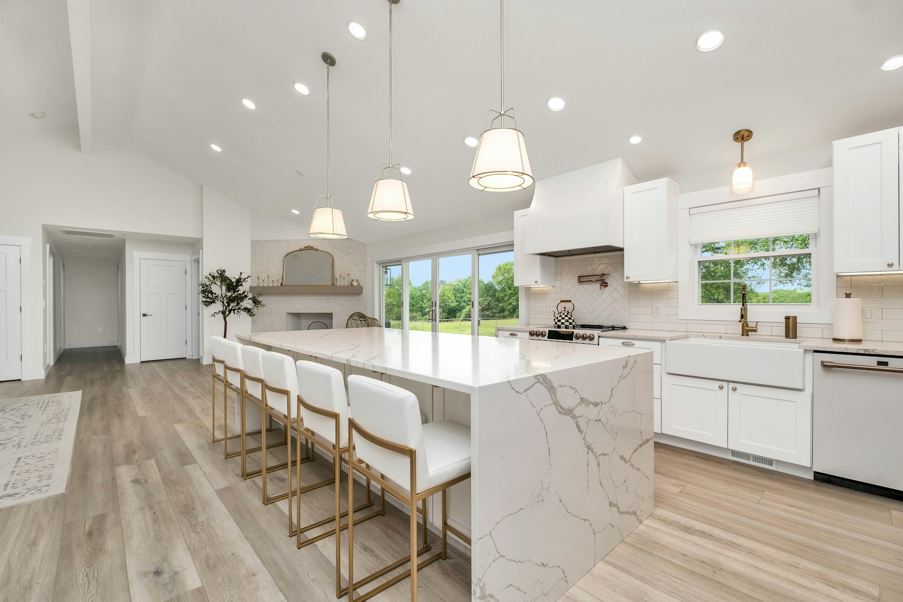 Finished kitchen with a marble waterfall island, white cabinets and pendant lights