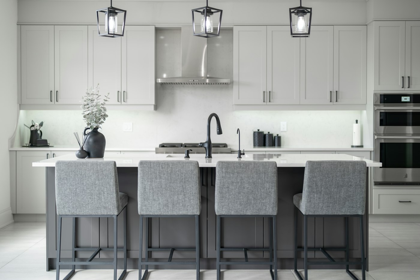 White kitchen with a grey island, pendant lights and bar stools