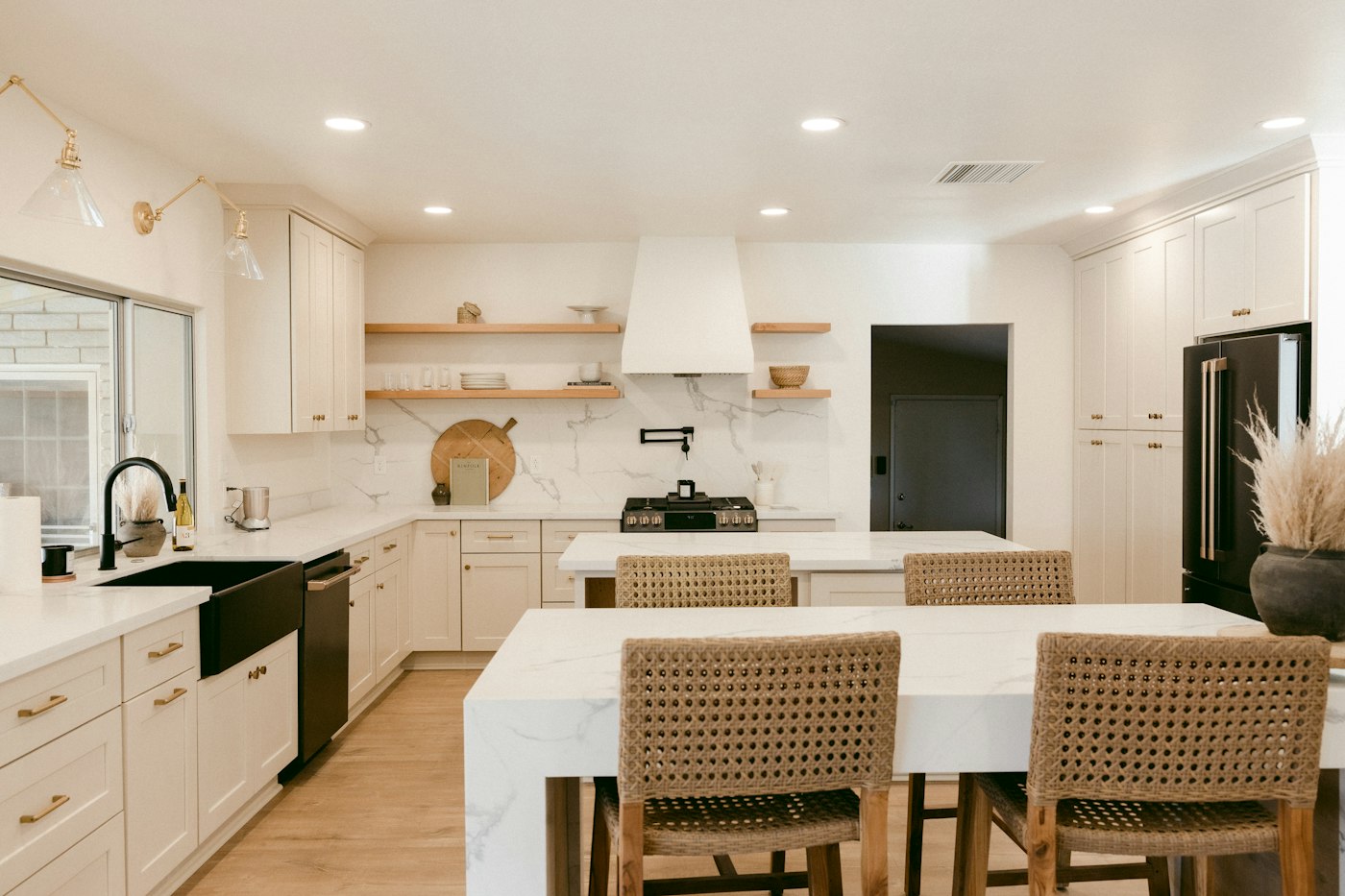 White farmhouse kitchen with a plaster range hood, open shelves and woven counter stools